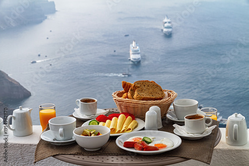 Morning breakfast table overlooking calm sea with cruise ships, coffee, bread, eggs, and juice in soft light.