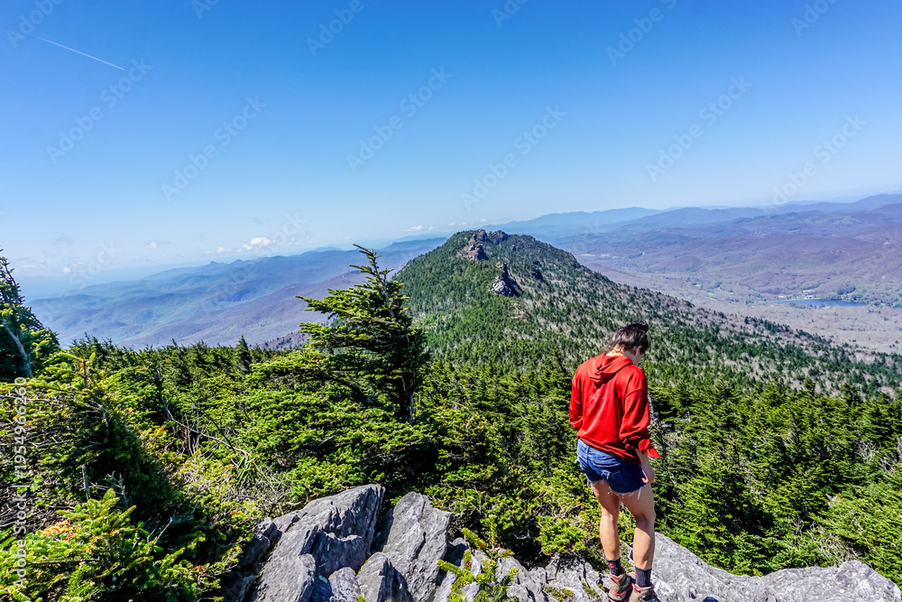 Fototapeta premium Hiker stands atop rocky peak, gazing at distant mountain range