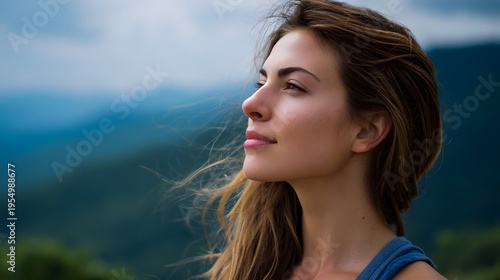 A young woman in profile looks upwards with a hopeful and contemplative expression against a backdrop of serene misty mountains