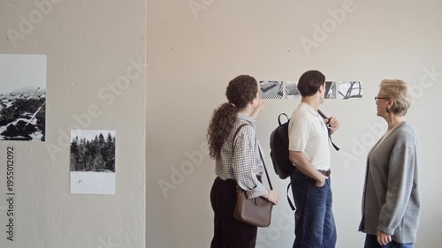 Tracking shot of confident mature Caucasian woman guiding young couple of gallery visitors through exhibition of black and white fine art photography