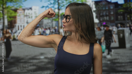 Tableau sur toile Young hispanic woman flexes bicep on sunlit city street; confidence empowerment strength motivation
