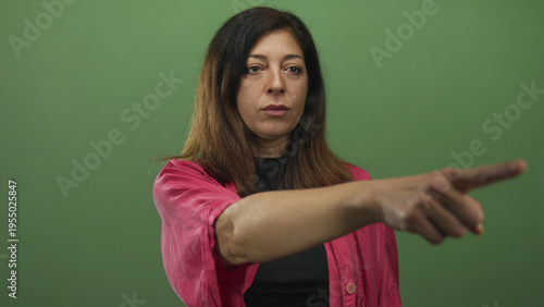 Fotografi Middle aged hispanic woman wearing pink shirt pointing finger at camera in green studio; confidence determination