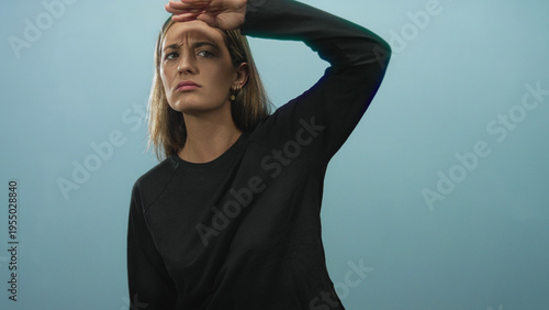 Photography Woman young blonde shielding eyes with hand and squinting while looking into distance in studio against pale blue backdrop; concern