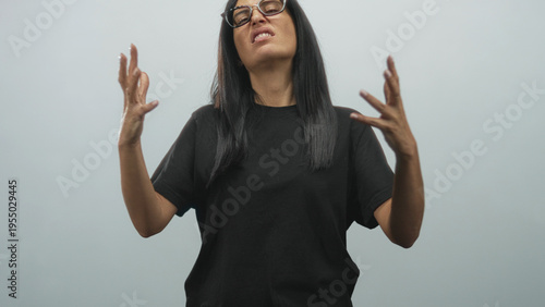Obraz na płótnie Woman with hands gesturing and grimacing teeth in studio wearing black shirt and glasses, speaking with expressive motion; exasperation