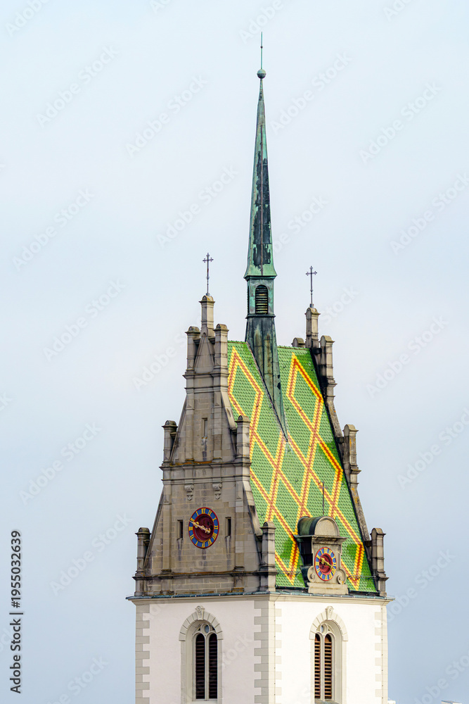 Obraz premium Old church tower with a green and yellow patterned roof stands against a cloudy sky in the afternoon