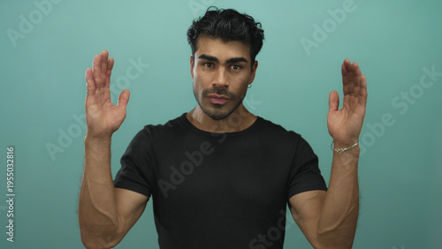 Photography Young hispanic man in black shirt raises open palms toward camera while smiling in studio; welcoming openness