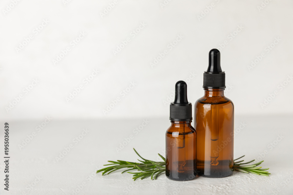 Fototapeta premium Rosemary essential oil on a textured background. Rosemary essential oil with fresh leaves nearby. Green rosemary sprig. Natural medicine, organic hair product, skin care, spa therapy. Beauty concept. 