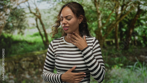 фотографія Woman holding throat with one hand and pressing upper abdomen with the other in a green forest park outdoors with breathing difficulty; discomfort