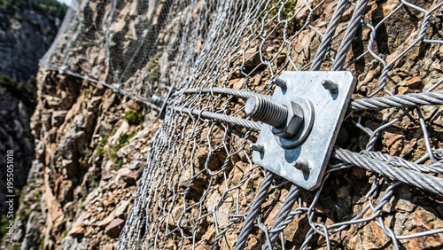 Close-up of heavy steel wire mesh bolted to a steep rock face for rockfall and landslide protection