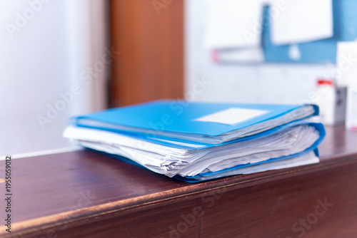 Close-up of organized medical history papers in a blue folder resting on a receptionist counter in a hospital. Administration and healthcare concept.
