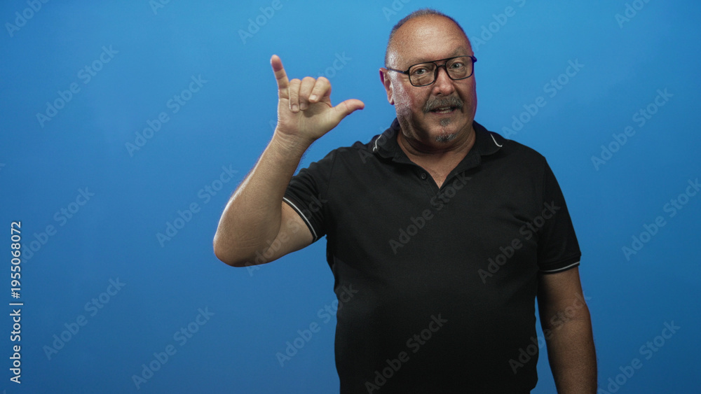 Fototapeta premium Man making hand sign with index and pinky raised and thumb extended in studio, wearing black polo and glasses; affection connection.