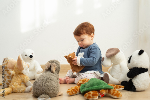 9-month-old baby girl sitting on the floor surrounded by plush toys and holding a stuffed fox.