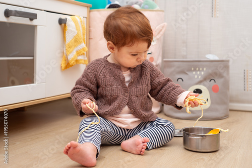 10-month-old baby girl playing with crochet spaghetti and a toy pot in a playroom.