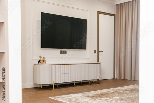 Modern living room interior with flat screen television mounted on white wall. Elegant media console with ribbed texture and gold accents. Stylish luxury home decor furniture design.