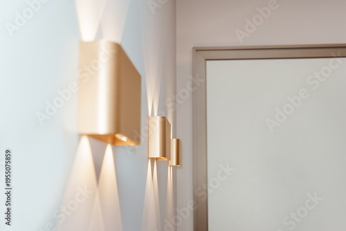 Modern wall lamps with glowing light beams in minimalist home interior. Stylish golden sconce on white wall for luxury house decor. Contemporary lighting design and architecture element.
