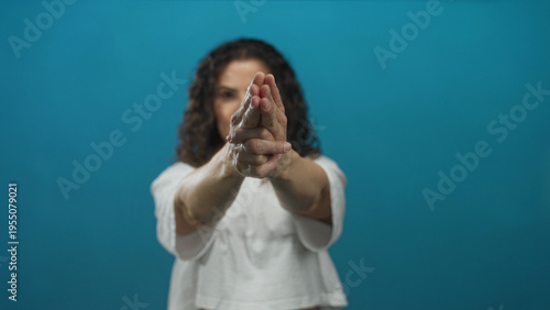 Fotografi Young hispanic woman makes pistol gesture with hands pointing at camera in blue studio; confidence