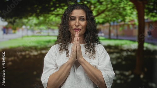 Cuadro en lienzo Woman with praying hands gesture in a leafy sunlit park with blurred building beyond; prayer faith serenity