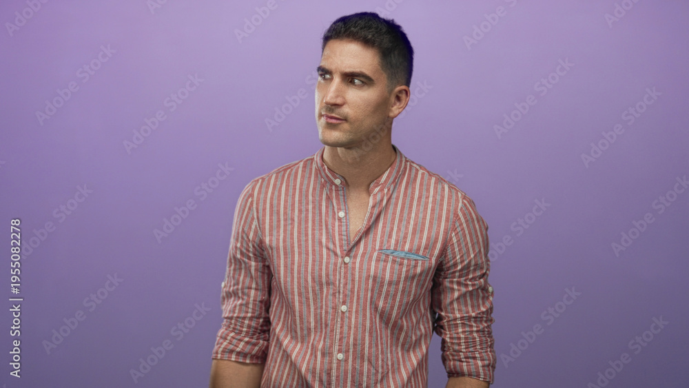 Fototapeta premium Man points finger to left in studio with purple backdrop, wearing striped shirt and leaning forward; surprise attention.