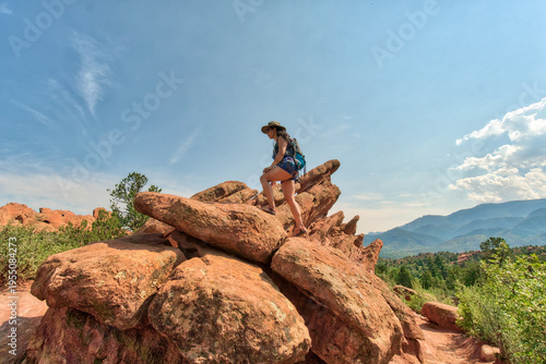 Woman stands atop rugged red rocks under a vast blue sky