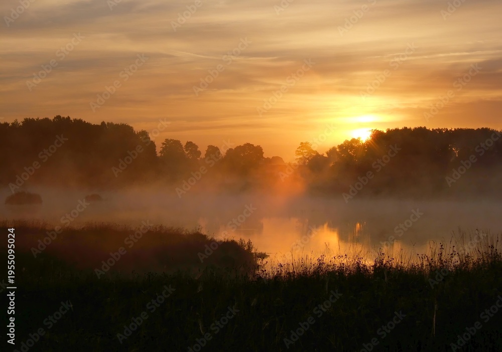 Obraz premium The sun rising over a misty forest and lake, creating a warm orange glow. Stunning morning landscape showcasing the beauty of Masurian nature.