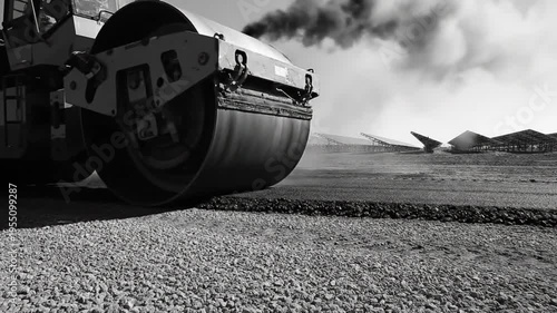 Black and white asphalt roller compacting freshly laid road surface with dark exhaust smoke billowing