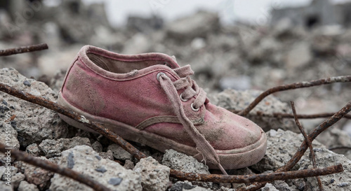A shot focuses on a single dusty pink canvas sneaker with white laces resting diagonally on a pile of rubble and rusted rebar