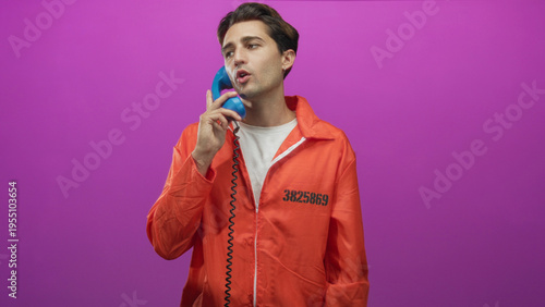 Photos Man in orange prisoner jumpsuit holds blue telephone handset to ear and gestures with hand in studio; remorse reflection
