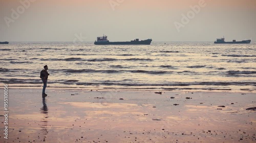 Mumbai Maharashtra India Jan 18 2026 A lone man stands at Juhu Beach during dark sunset facing the Arabian Sea with distant ships and wet sand reflections creating a calm moody coastal atmosphere.