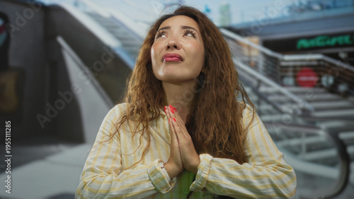 Fotografie Woman with hands pressed together praying in mall center shop indoors looking upward at ceiling; hope prayer