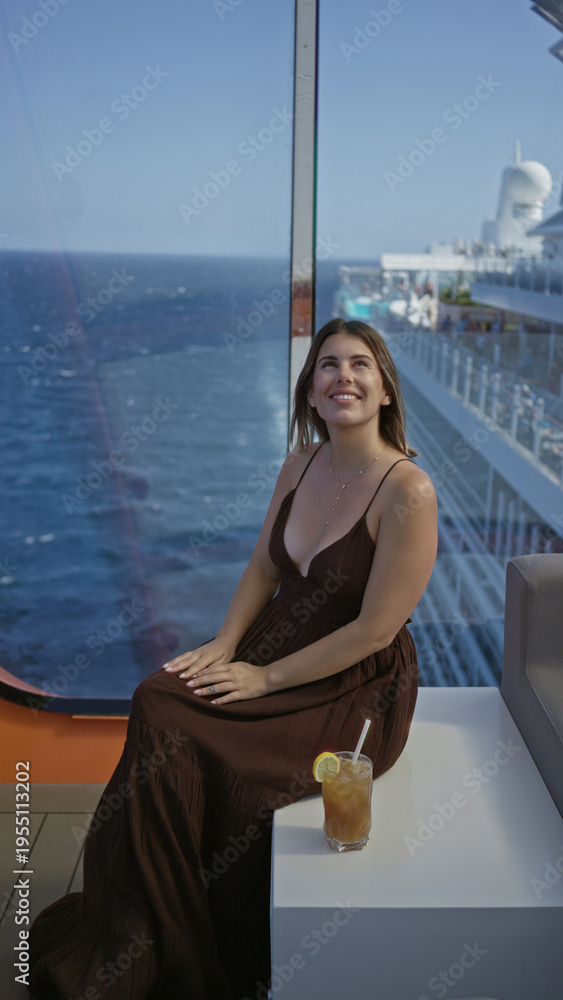 Fototapeta premium Woman smiling and sitting showing cleavage on cruise ship terrace with ocean view and drink nearby; relaxed serenity.