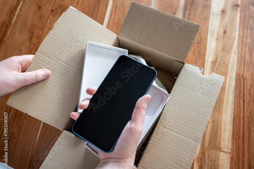 Hand holding new mobile phone after delivery. Unpacking the box with smartphone.