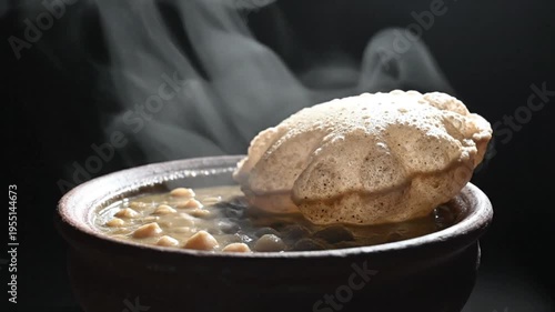 Steaming bowl of Indian chana masala with puffed puri bread, traditional vegetarian cuisine