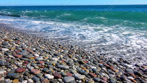 Waves Crashing on a Pebble Beach with Clear Blue Water and a Bright Sunny Day along the Coastline