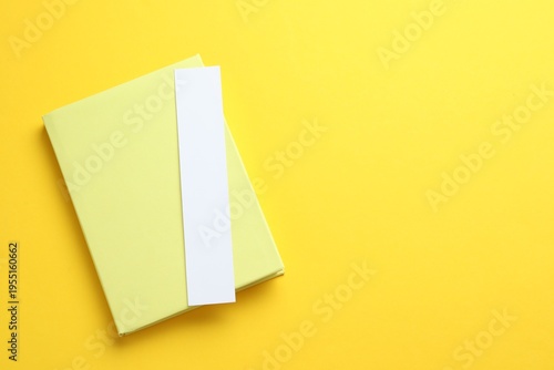 Book with white bookmark on yellow background, top view. Space for text