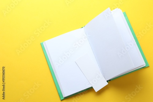 Book with white bookmark on yellow background, top view. Space for text