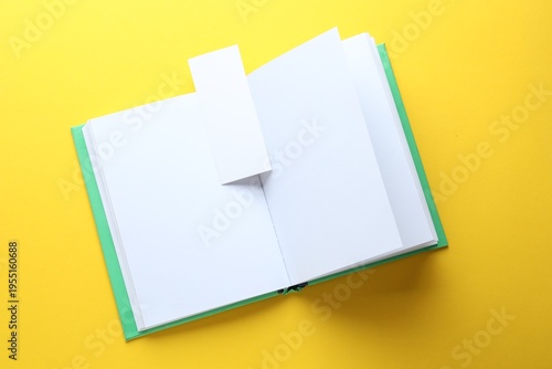 Book with white bookmark on yellow background, top view