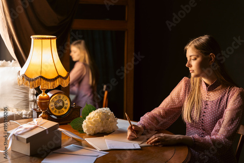 Billede på lærred A young woman sits at a wooden desk, writing a letter in the warm glow of a vintage lamp