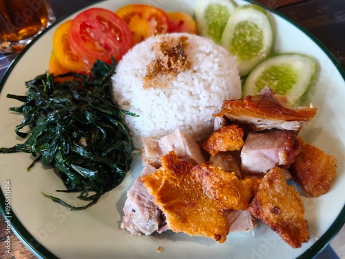 Plated rice with crispy pork, greens, and fresh vegetables