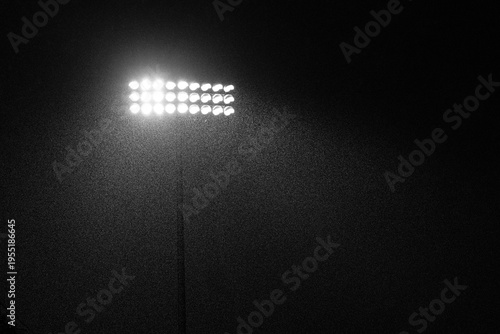 Bright illuminated stadium lights at night during a rainstorm. Great texture and mood with directional lighting. Strong, dramatic image of a sporting event