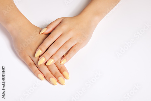 Schilderij op canvas Close-up of female hands with soft pastel yellow manicure on a clean neutral background