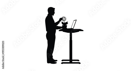 Silhouette of a man standing at an adjustable desk, working on a laptop and watering a plant