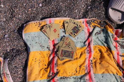 Playing cards spread on a striped beach towel with pebbles scattered around