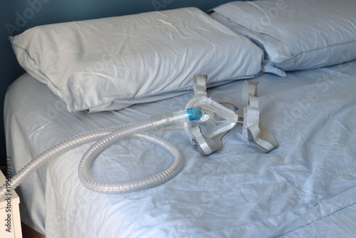 A close-up view of a CPAP mask and its corrugated tube lying on a blue-sheeted bed, suggesting sleep therapy or medical care at home