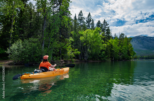 Woman kayaking on clear mountain lake surrounded by forest and scenic landscape, outdoor adventure and peaceful nature concept