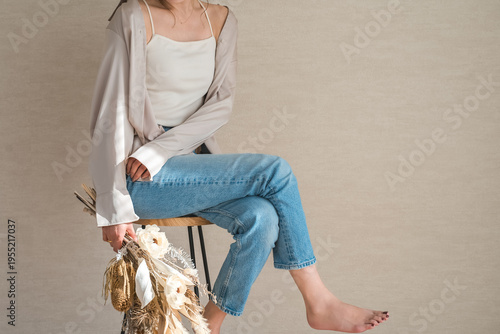 Fotografía A stylish denim-clad female model sits on a chair, holding a swag or bouquet of flowers
