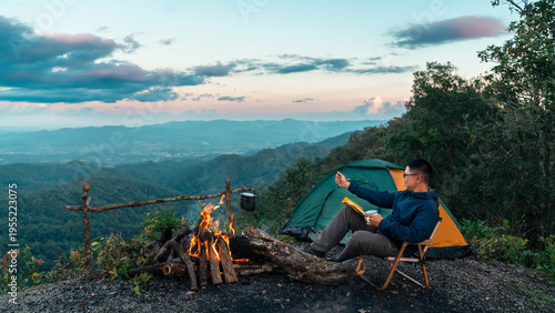 Bild auf Leinwand Asian man camping in forest writing travel journal beside campfire, outdoor adve