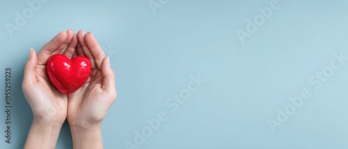 Hands holding a red heart on a light blue background, symbolizing love, care, and health.