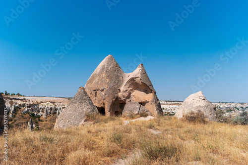 Wallpaper Mural Goreme, Nevsehir, Turkey. Landscape with two prominent rock dwellings carved into formations, dry grass and shrubs in foreground, clear blue sky, serene and picturesque scene. Torontodigital.ca