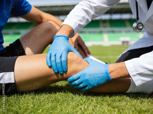 A medical professional in blue gloves examines a patient's knee injury on a sports field, indicating athletic first aid.