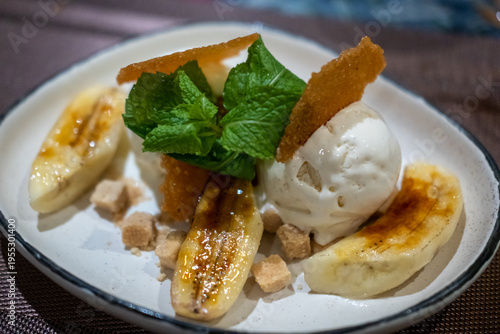 Caramelized banana dessert served with vanilla ice cream, mint leaves, and crispy sugar garnish on a plate.